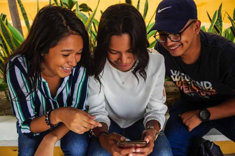 two women and a man smiling while looking at a phone