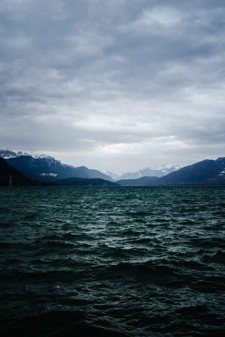 body of water near mountain under cloudy sky