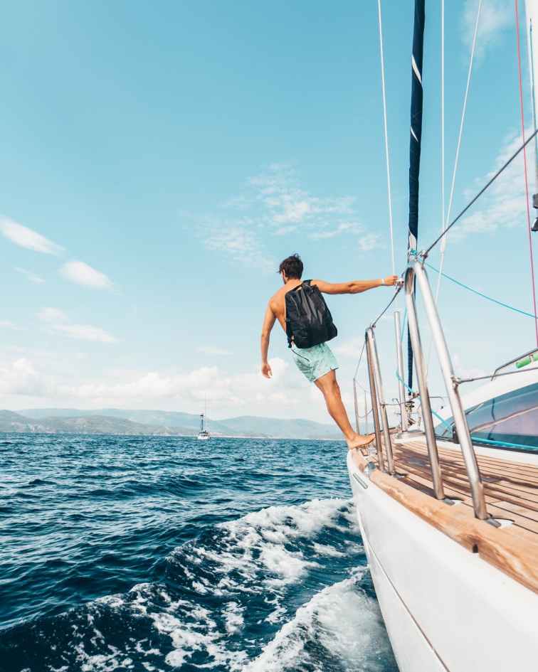 man wearing backpack standing on side of boat during daytime