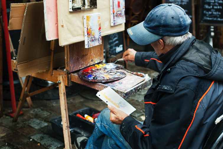 man holding brush while painting in front of easel