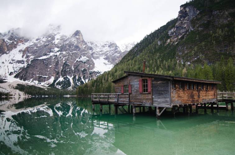 brown wooden house on lake near snow covered mountain