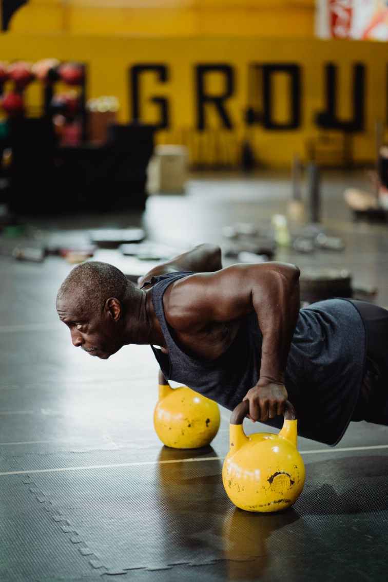 photo of man doing push ups using yellow kettlebell